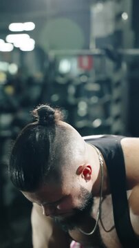 Intense close-up of a muscular bearded athlete with a man bun grinding through a heavy gym workout under dramatic backlighting, showcasing strength, sweat, and determination