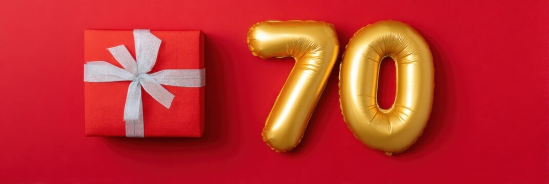 Golden number 70 balloon and red gift box with silver ribbon on red background