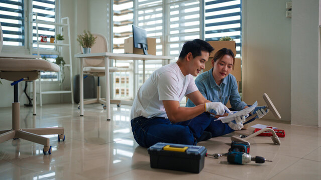 Asian adult couple assembling furniture at new home DIY project teamwork relocation moving house apartment setup instruction manual reading home improvement