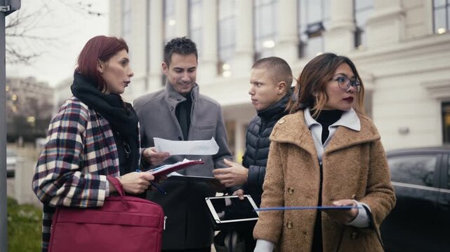 Four young professionals hold an impromptu outdoor business meeting, discussing plans and documents.