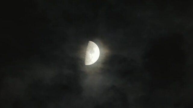 A waxing moon in the night sky and flying clouds. Cloudy dark sky and moonlight
