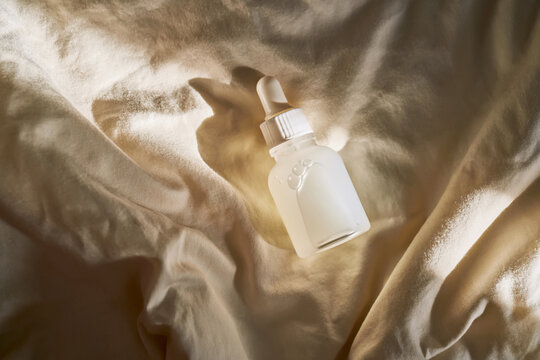 Skincare serum bottle on fabric in morning light