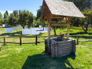Rustic wooden well in countryside garden with laundry drying in summer.