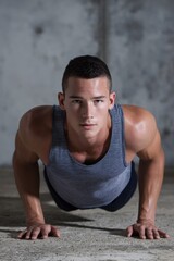 Obraz premium Young caucasian male performing push-ups for fitness in grey tank top