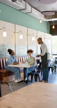 Vertical video: African American women watching male server in apron showing reader to pay at cafe