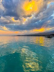 Fototapeta premium Sunset at Issyk Kul Lake in Kyrgyzstan. Bright sun breaking through clouds reflecting in clear turquoise water.