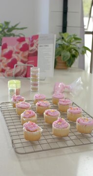 Vertical video: Camera pulling back to show rack holding pink cupcakes and piping bag on counter