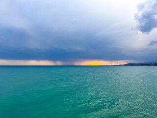 Fototapeta premium Sunset at Issyk Kul Lake in Kyrgyzstan. Bright sun breaking through clouds reflecting in clear turquoise water.