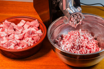 Ground pork in stainless steel bowl against household meat grinder