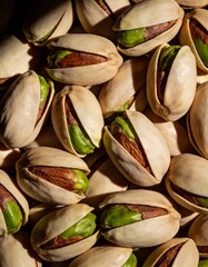 Abundant natural pistachios in their shells, some partially open to reveal vibrant green nuts, with dramatic lighting creating a rich, textured, and appetizing background.