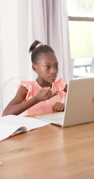 Vertical video: African child in pink top watching laptop lesson, counting on fingers with notebook