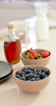 Vertical video: Camera panning on counter, revealing pink berry bowls, syrup bottle and milk carafe