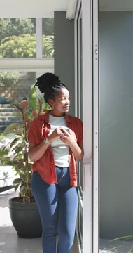 Vertical video: African American woman holding phone by glass door, phone buzzing, glancing outside