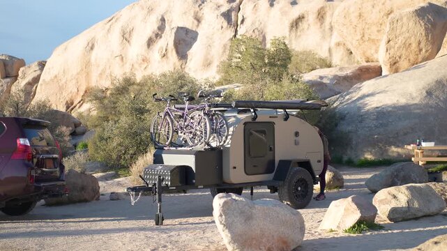 Suv parks next to teardrop camper trailer at campsite in Joshua Tree National Park during sunny day.