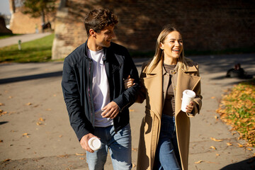 Obraz premium Couple enjoying walk while holding coffee cups on sunny day in park