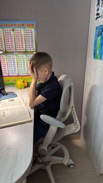 A tired boy sits at his desk with his head in his hands struggling with homework near a math poster, stressful learning moment, educational challenge.