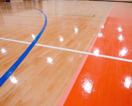 Polished wooden floor of a sports hall with colorful marking lines for basketball and volleyball competition, indoor gym stadium architectural background with copy space