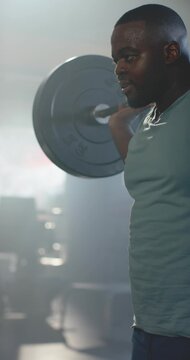 Vertical video: Adult African American man bracing, doing barbell squat training in gym, copy space