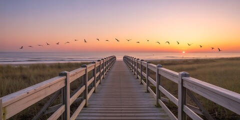 Fototapeta premium Wooden boardwalk leading to beach at sunset with birds flying overhead ocean view