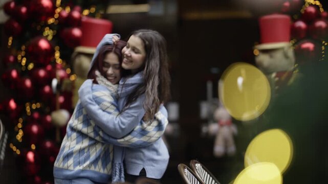 Two young girls share a heartfelt hug outdoors during the Christmas holiday season. Friends embrace joyfully amidst festive decorations and winter cheer.