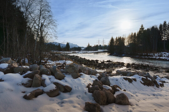 Scenic winter landscape of the Lech river with snow-covered rocks, animal tracks, and distant Alpine mountains in Bavaria