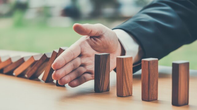 Businessman stopping falling dominoes with his hand