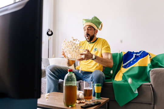 Brazilian football fan watching match at home while supporting national team. Emotional sports moment showing excitement, anticipation and entertainment lifestyle during televised competition.