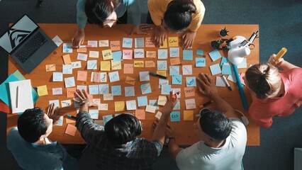 Top down view of skilled marketing team using sticky note to share idea. Aerial view of group of business people working together to brainstorm idea while taking a note to plan strategy. Symposium. © InfiniteFlow