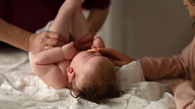 Baby lying on their back while an adult massages them and the mother holds the pacifier in the baby's mouth