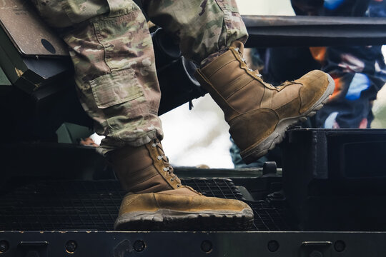 Close-up of a soldier in camouflage pants and tactical desert boots sitting on an armored vehicle during a military mission