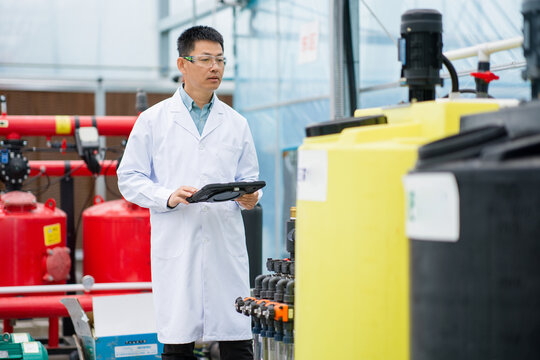 Scientist in lab coat holding tablet while inspecting industrial equipment in facility