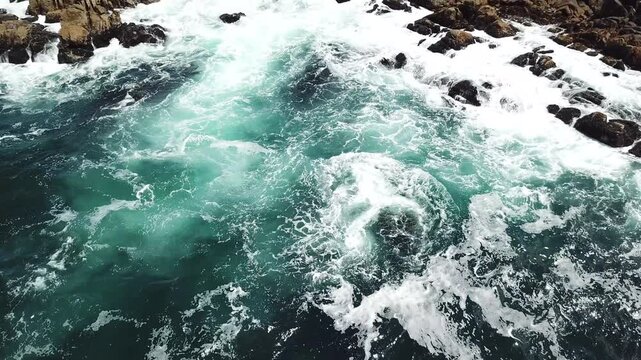 The aerial drone captured Montereys coast, exposing its rugged cliffs shaped by the relentless waves.  The dramatic landscape as the waves create an intricate pattern.