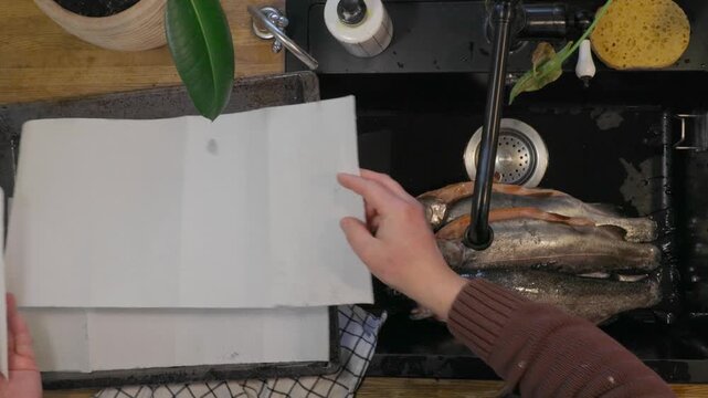 Top view of man cleaning and preparing fresh fish in black kitchen sink. Home seafood preparation process before cooking, everyday kitchen routine and food preparation concept