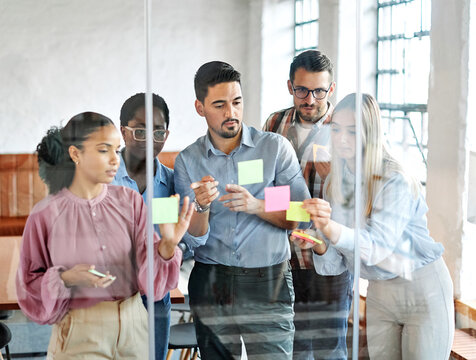Business people meeting at office and using sticky notes on glass to share idea. Brainstorming and teamwork concept. Sticky note on glass wall.