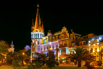 Obraz premium Ornate historic theater architecture in Batumi brightly illuminated at night with palm trees and city lights in warm evening atmosphere