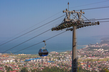 Modern cable car gondola high above Batumi city with industrial port tanks and Black Sea coastline visible in clear daytime atmosphere © Kavalenkava