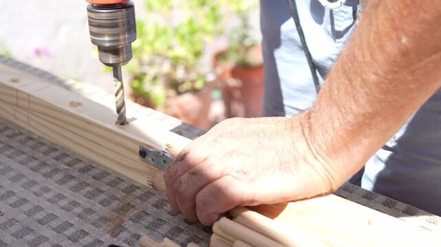 Hands working wood with a drill on an outdoor table.