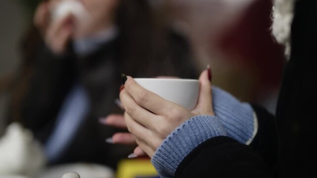 Close-up on the hands of a carefree girl holding a steaming cup of tea. Her hands are warming around the hot beverage during a relaxed moment.