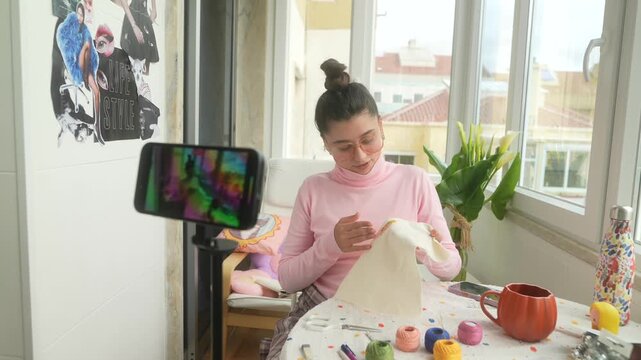 Young woman documents needlework at sunny window with equipment