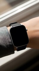 Fototapeta premium A person's hand wearing a black square smartwatch against a blurred background of a window