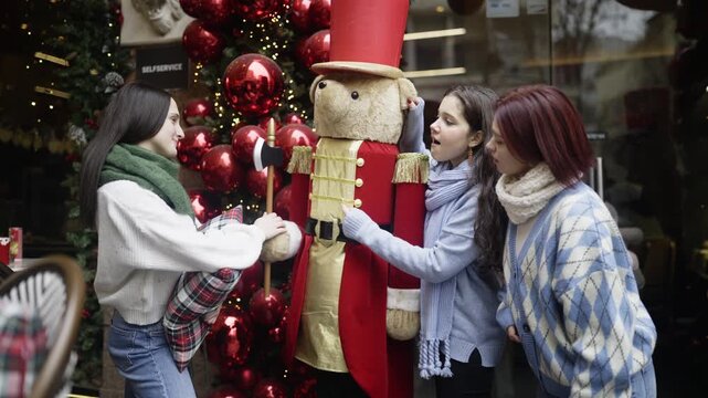 Three carefree friends interact playfully with a festive nutcracker bear decoration during the winter holidays.