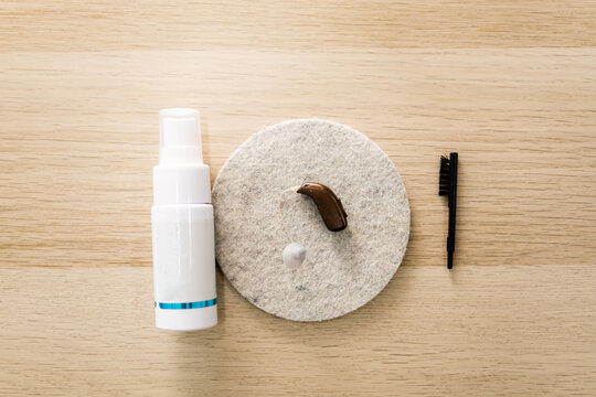 Overhead photograph of a hearing aid with cleaning products such as soap or a brush. Concept of cleaning hearing aids or earphones.