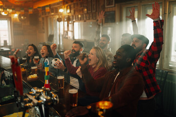 Diverse friends cheering loudly watching sports in pub