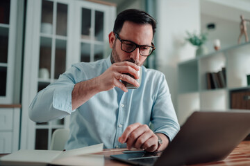 Professional man working remotely from home on laptop, drinking coffee and planning strategy