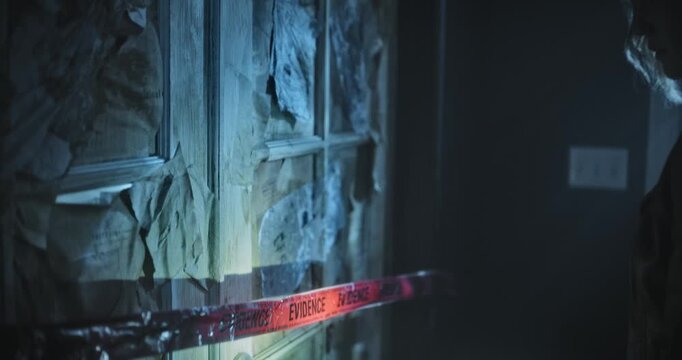 Young woman with flashlight pulling red tape off spooky door in dark house and entering - medium, side shot