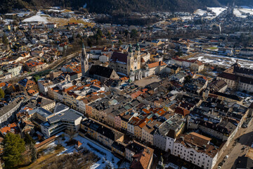 Aerial view of Brixen, Italy, shows Brixen Cathedral twin towers, Gothic bell tower, pastel facades, red roofs, cathedral square, winter hills, and long shadows.