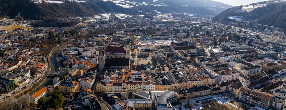 Aerial view of Brixen, South Tyrol, shows Brixen Cathedral, twin towers, red roof, pastel facades, Eisack River, small bridges, Alpine hills, and crisp winter light.