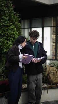 Two dedicated teenagers are seen concentrating on their notebooks, actively writing and drawing outdoors. They appear to be collaborating on a creative project or diligently studying together.