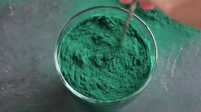 Stirring green spirulina algae powder in a glass of water