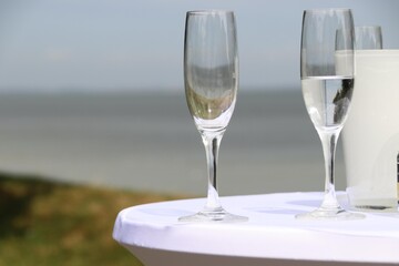 Glasses and sparkling wine on a white standing table on the beach create a festive atmosphere,...
